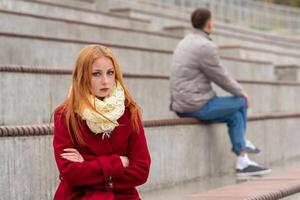 young couple in a quarrel, a guy and a girl are sitting far from each other in the empty stands photo