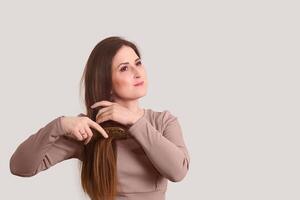 joven mujer peinada su largo Derecho pelo con un peine en un ligero antecedentes foto