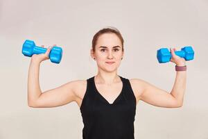 young woman performs an exercise with dumbbells, half-length portrait on a light background photo
