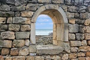 ventana apertura en el restos de un antiguo muro, detrás cuales usted lata ver el mar foto
