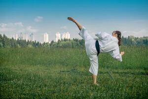 Adolescente niña formación kárate kata al aire libre, realiza el uro mawashi geri gancho patada foto