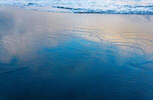 Oceano playa con un ola viniendo atrás, en cuales el cielo es reflejado foto