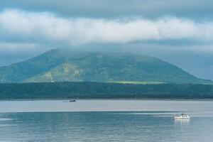 waterscape of the sea bay with a fishing ship and a mount in the clouds in the background, a view of the Mendeleev volcano from the side of the town of Yuzhno-Kurilsk photo