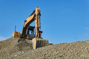 excavator standing on a pile of rubble against the sky photo