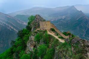 ancient tower and castle wall on top of a sheer cliff in a mountainous area, Gunib Shamil fortress in Dagestan, photo