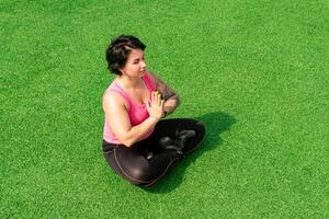 young sturdy chubby woman meditates on the lawn after exercising photo