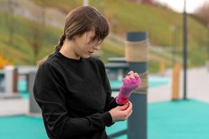 young woman wrapping a wrist wrap around her hand before outdoor martial arts training photo