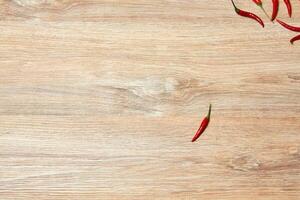 single pod of red chili pepper lies on a wooden surface away from a group of other fruits photo