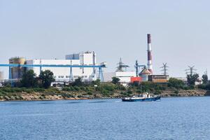 industrial landscape with a factory on the banks of the river, along which a motorship floats photo