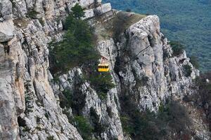 cabin of the aerial tram moves against the background of a steep rocky cliff photo