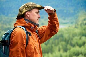 traveler looks into the distance from under the arm against the backdrop of a wooded mountain landscape photo