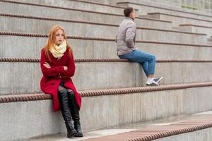 young couple in a quarrel, a guy and a girl are sitting far from each other in the empty stands photo