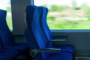 interior de viajero diario al trabajo pasajero tren auto, fila de sillas y un movimiento borroso paisaje fuera de el ventana foto