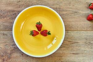 Tres fresas en un amarillo plato en un de madera mesa foto