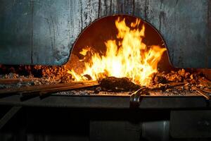 herrero horno con ardiente fuego con palanquillas calefacción en eso foto