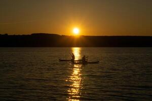 two surfers on standup paddleboards against the backdrop of the setting sun photo