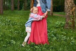 contento niño niña abrazos su mamá en pie en el césped en el parque foto