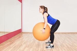 young woman is training by doing squats with fyt ball in gym photo