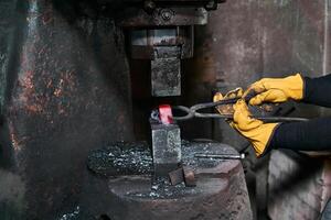 hembra manos procesos un rojo caliente pieza de trabajo con un poder martillo foto