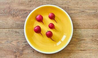 cinco rojo rábanos en un amarillo plato en un de madera mesa foto