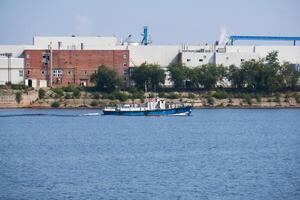 industrial landscape with a factory on the banks of the river, along which a motorship floats photo