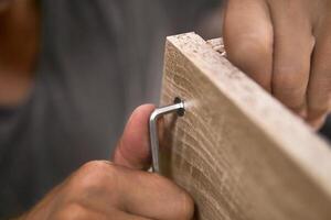 man assembles furniture by hand, focus on fastener and hex key in his fingers photo