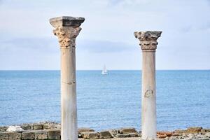 dos arruinado antiguo columnas en contra el antecedentes de el mar, dónde usted lata ver un borroso navegación Embarcacion foto