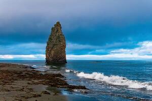 seascape of Kunashir, ocean shore with a huge vertical rock in the water and a wild beach with algae thrown out by the sea photo