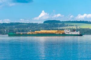 cargo ship loaded with lumber follows a wide river on a sunny day photo