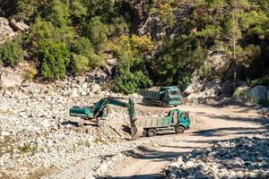 road works in the river valley, excavator and dump trucks move stones photo