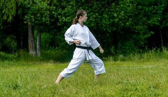 teenage girl training karate kata outdoors, performs gedan-barai or downward block photo