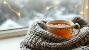 AI generated A cup of hot tea warmed in the knitted scarf is on the windowsill against the winter window photo