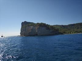 Blue sea and rocks, a ship is sailing on the horizon photo