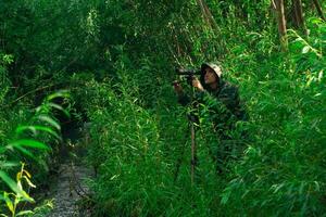 man wildlife explorer makes field observation with a spotting scope among the thickets in a river valley photo