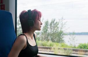 girl with headphones rides in a moving suburban train and looks out the window photo