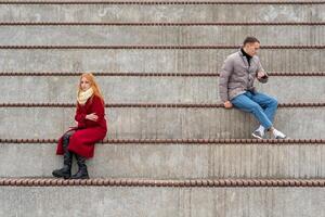 young couple in a quarrel, a guy and a girl are sitting far from each other in the empty stands photo