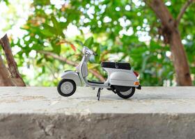 Miniature classic scooter on the cement floor with nature background. After some edits. photo