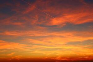 airplane and its trail in the sky. clouds and different color tones in the sky at sunset. Amazing and incredible sunset. photo