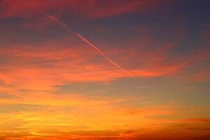 airplane and its trail in the sky. clouds and different color tones in the sky at sunset. Amazing and incredible sunset. photo