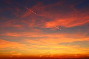 airplane and its trail in the sky. clouds and different color tones in the sky at sunset. Amazing and incredible sunset. photo