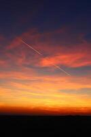 airplane and its trail in the sky. clouds and different color tones in the sky at sunset. Amazing and incredible sunset. photo