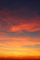 airplane and its trail in the sky. clouds and different color tones in the sky at sunset. Amazing and incredible sunset. photo