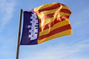 A vibrant flag with red and yellow stripes along a blue background with an emblem, against a blue sky, Majorca, Balearic Islands, Spain. photo