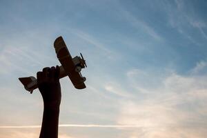 Child Holding a Wooden Airplane Model High in the Sky photo