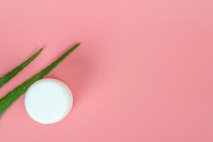 Fresh aloe vera leaves and white plastic cosmetic jar on pastel pink background for Health and beauty products. photo