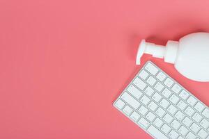 Flat lay, top view office table desk. Workspace with keyboard and hand Sanitizer on pink background. photo