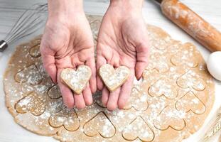 Woman's hands holding two hearts made from dough. Homemade pastry. Cooking process. Close-up. Top view. photo