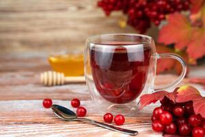 Healthy and tasty tea from viburnum berries in glass cup on a wooden table. Seasonal drink. Close-up. Copy space. Selective focus. photo