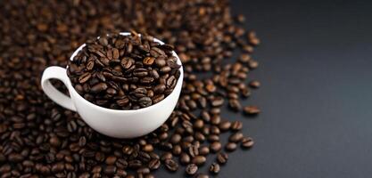 Fresh aromatic coffee beans in a white cup on a black background. Banner. Place for text. Selective focus. photo