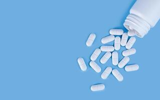 Scattered white pills from the white bottle on blue background. Health care and medicine concept. Close-up. Place for text. photo